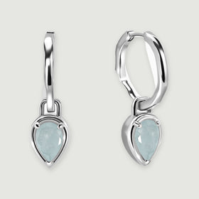 Two polished silver-tone hoop earrings with pale blue pear-shaped aquamarine drops rest on a light gray background.