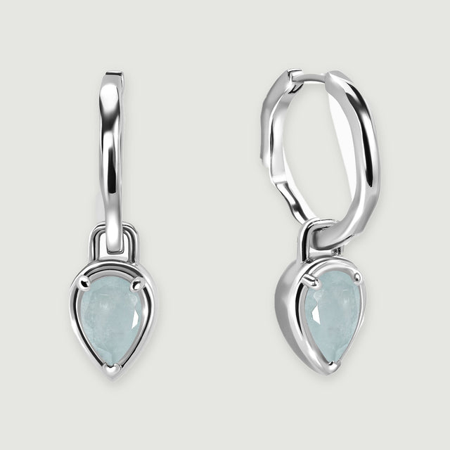 Two polished silver-tone hoop earrings with pale blue pear-shaped aquamarine drops rest on a light gray background.
