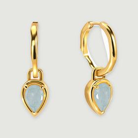 A pair of yellow gold-tone hoops with pale blue aquamarine drops is centered above soft shadows.