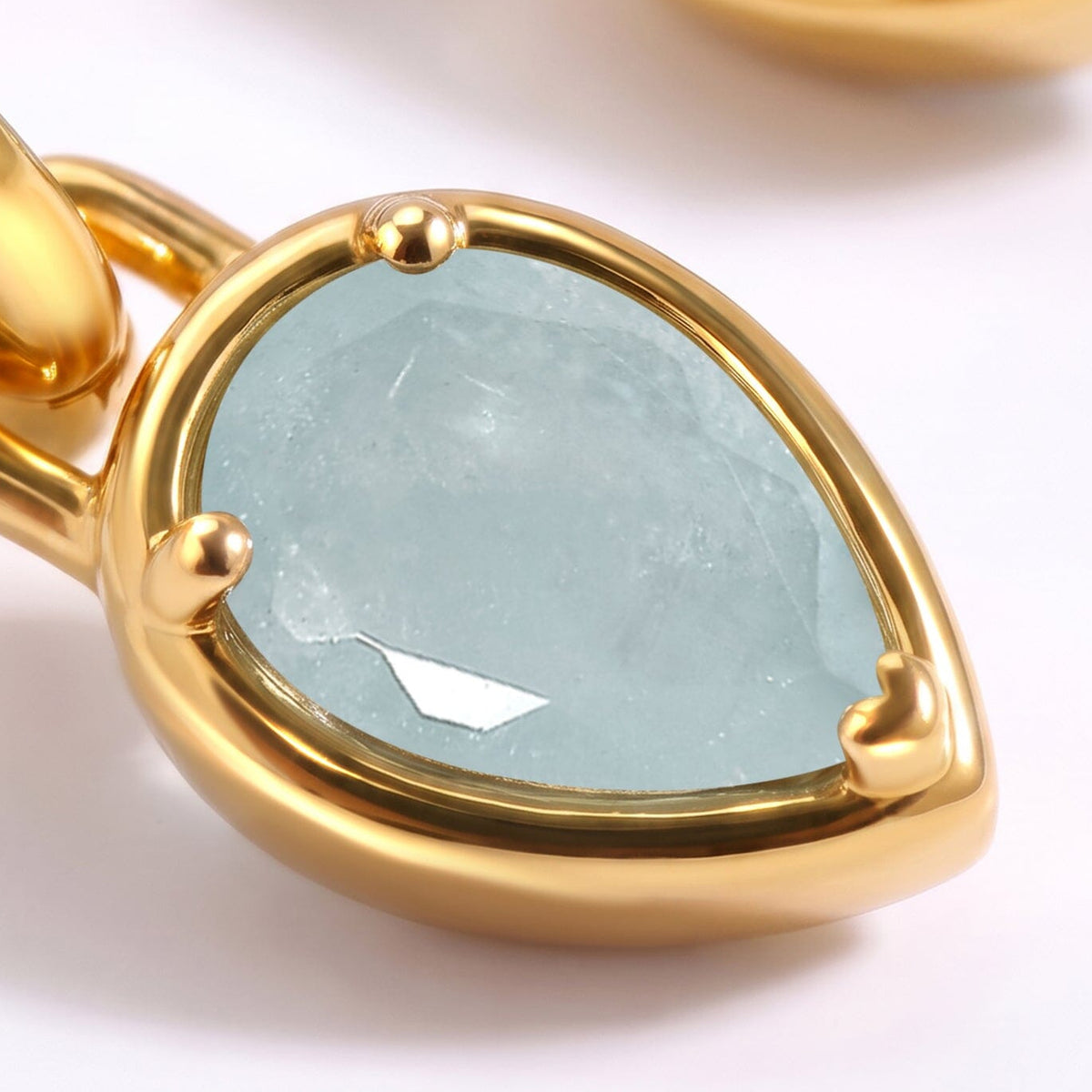 Facets and pale blue inclusions are visible within an aquamarine drop framed by yellow gold-tone metal.