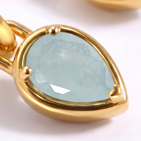 Facets and pale blue inclusions are visible within an aquamarine drop framed by yellow gold-tone metal.