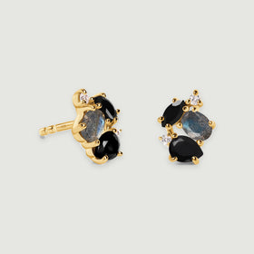 Two yellow gold vermeil stud earrings display black gemstones, oval blue gray stones and clear accents with soft shadows beneath them.