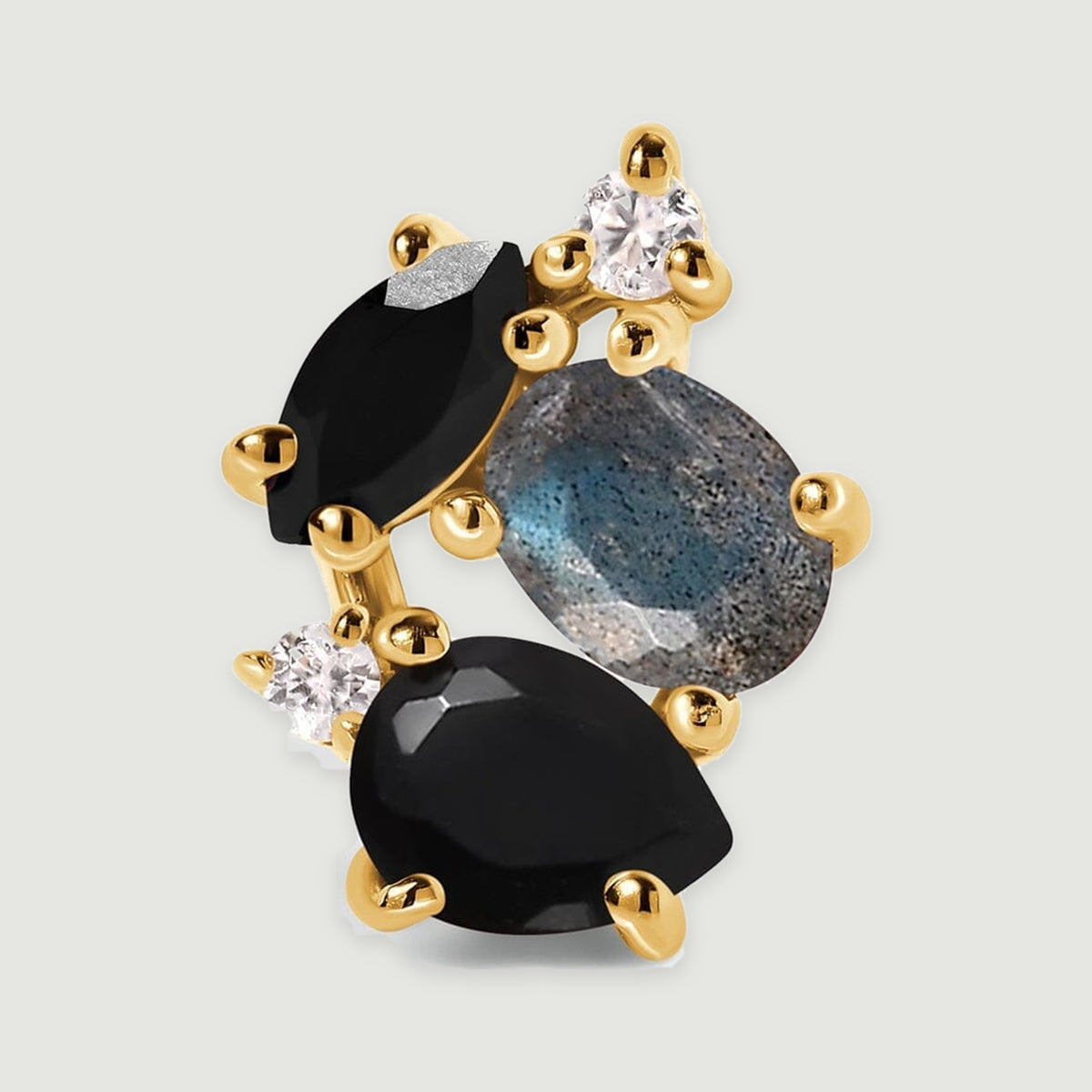 A close view of a yellow gold vermeil stud earring reveals polished prongs surrounding black and blue gray gemstones.