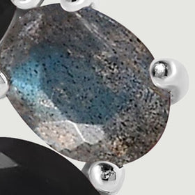 A tight detail shows the blue gray oval gemstone, its mottled surface and polished silver prongs beside a black faceted stone.