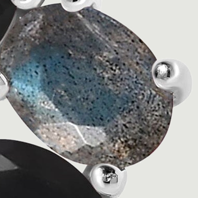A tight detail shows the blue gray oval gemstone, its mottled surface and polished silver prongs beside a black faceted stone.