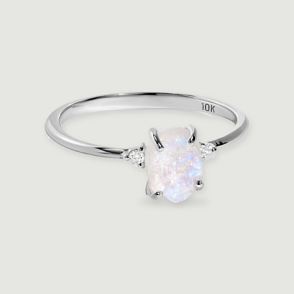 A white gold ring displays an irregular moonstone between two small round diamonds against light gray.