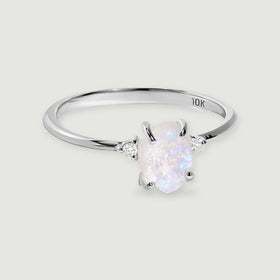 A white gold ring displays an irregular moonstone between two small round diamonds against light gray.