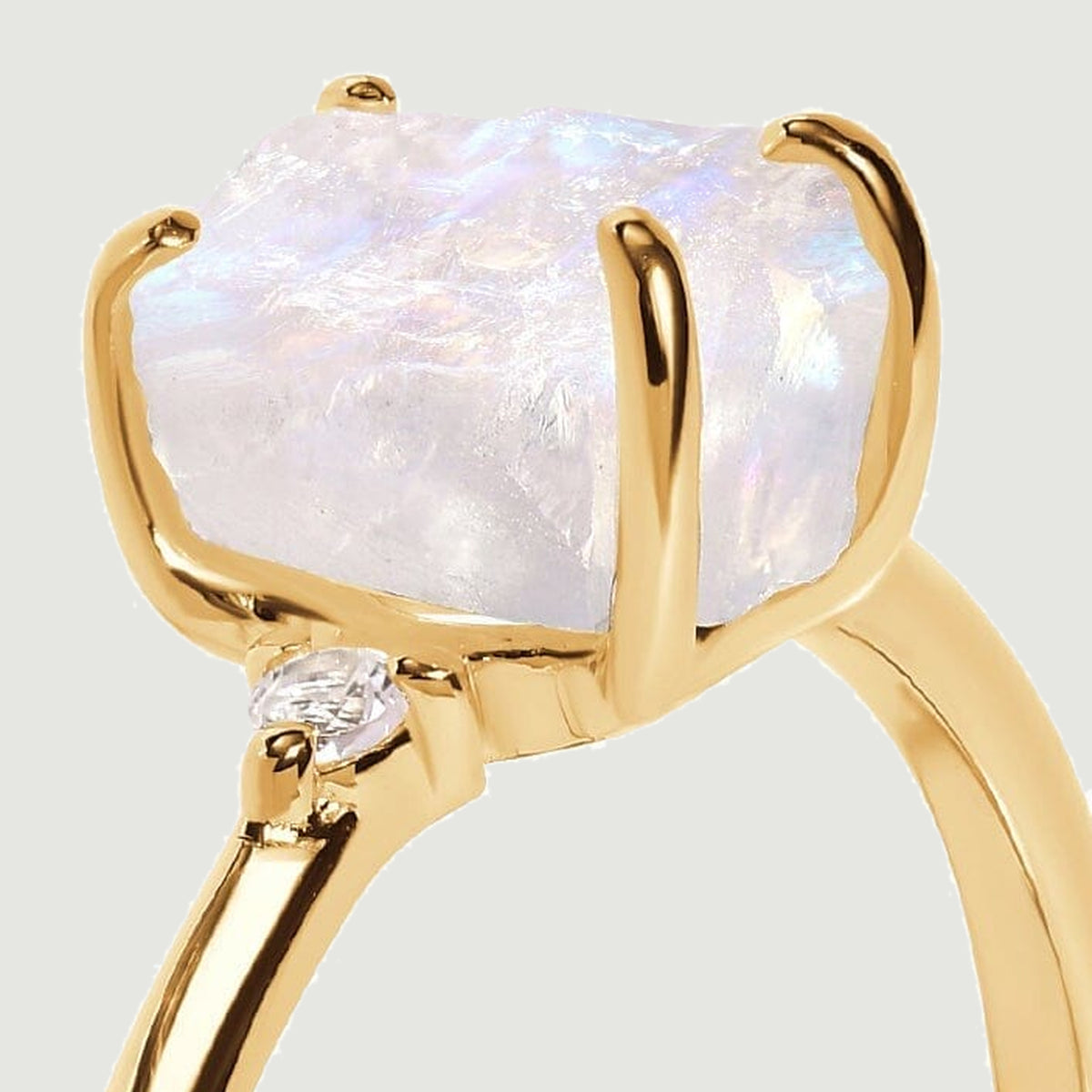 The yellow gold prongs hold a rough moonstone above a diamond accent in this close side view.