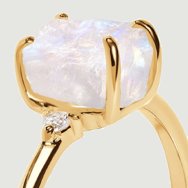 The yellow gold prongs hold a rough moonstone above a diamond accent in this close side view.