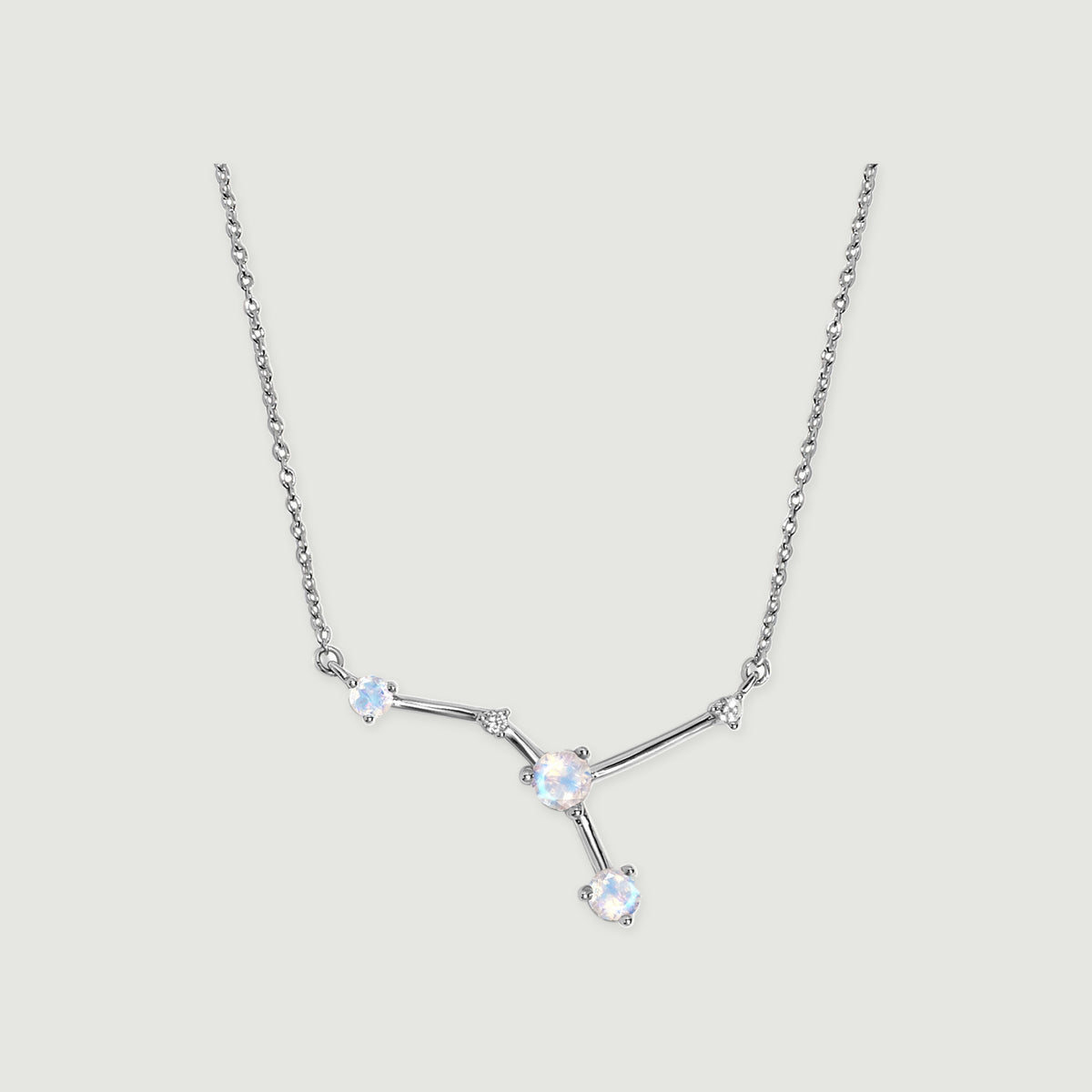A sterling silver chain frames three pale round stones and two small clear accents on a light gray background.