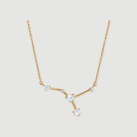 A yellow gold vermeil necklace has polished angular bars joining pale faceted stones against a gray surface.