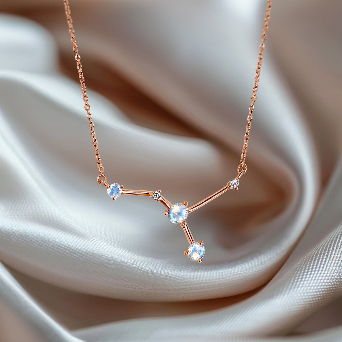The rose gold vermeil necklace lies over folds of cream fabric with three pale stones facing upward.