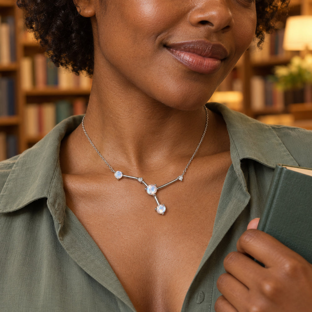 A woman in a sage green shirt wears a silver necklace while holding a green book in a softly lit bookshop.