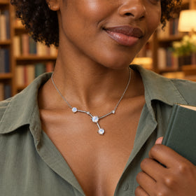 A woman in a sage green shirt wears a silver necklace while holding a green book in a softly lit bookshop.