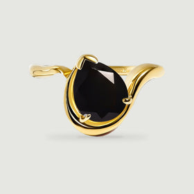 A pear-shaped black stone rests in a curved yellow gold ring on a light gray surface.