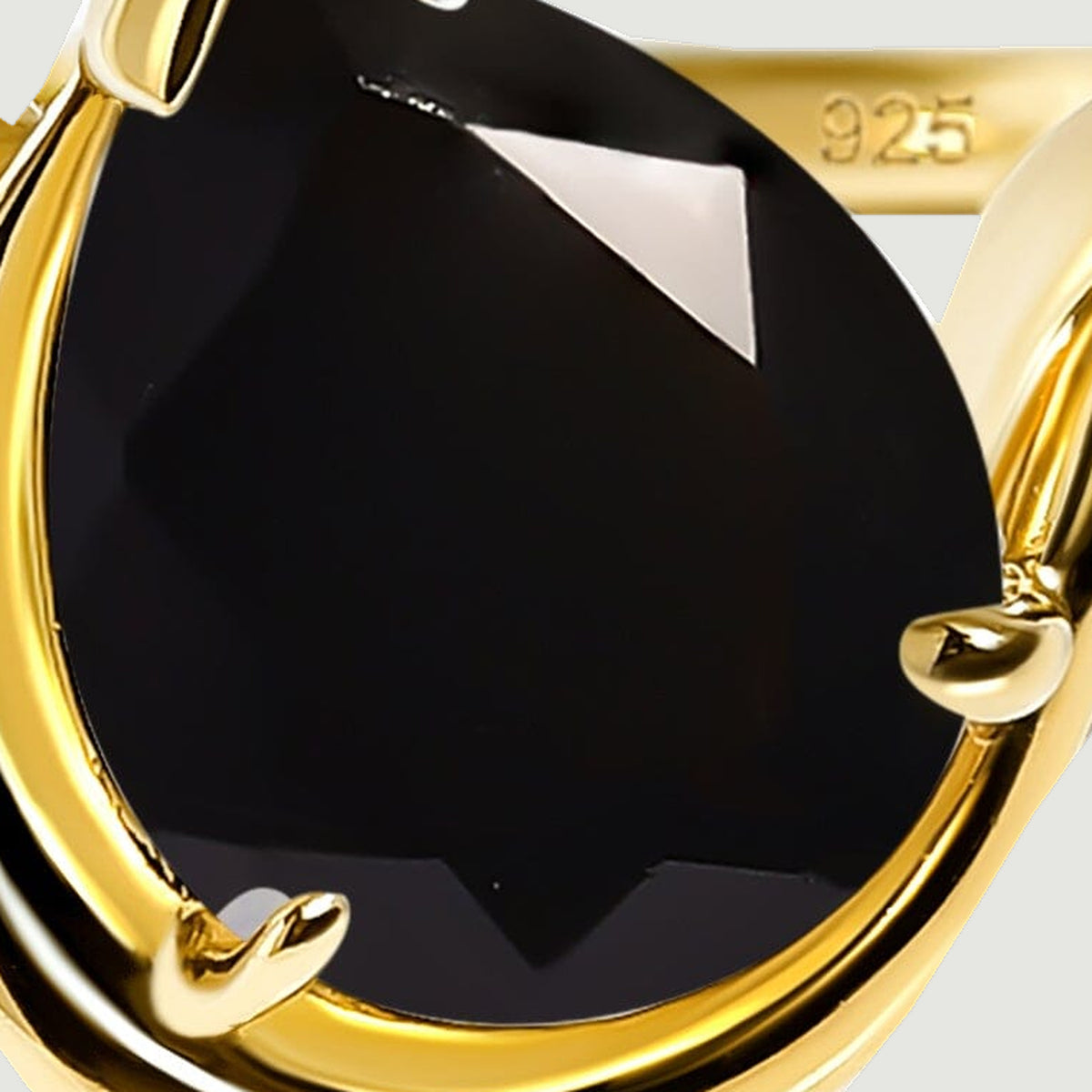 The glossy black pear-shaped stone shows angular facets inside its yellow gold setting.