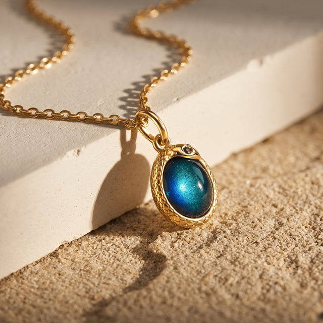 A yellow-gold-toned chain lies across a cream stone block while the blue-green pendant catches warm light.