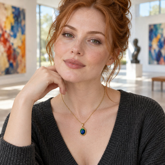 A red-haired woman in a charcoal knit top wears a yellow-gold-toned oval pendant in a bright art gallery.