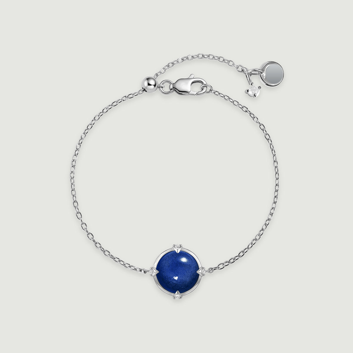 A silver tone bracelet forms an oval around its blue round stone, with its clasp and extension chain visible above.