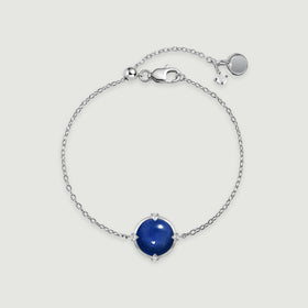 A silver tone bracelet forms an oval around its blue round stone, with its clasp and extension chain visible above.