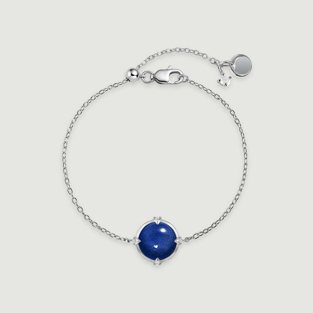 A silver tone bracelet forms an oval around its blue round stone, with its clasp and extension chain visible above.