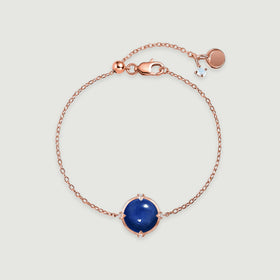 A rose gold tone bracelet with a glossy blue cabochon, delicate links, and a lobster clasp rests on pale gray.