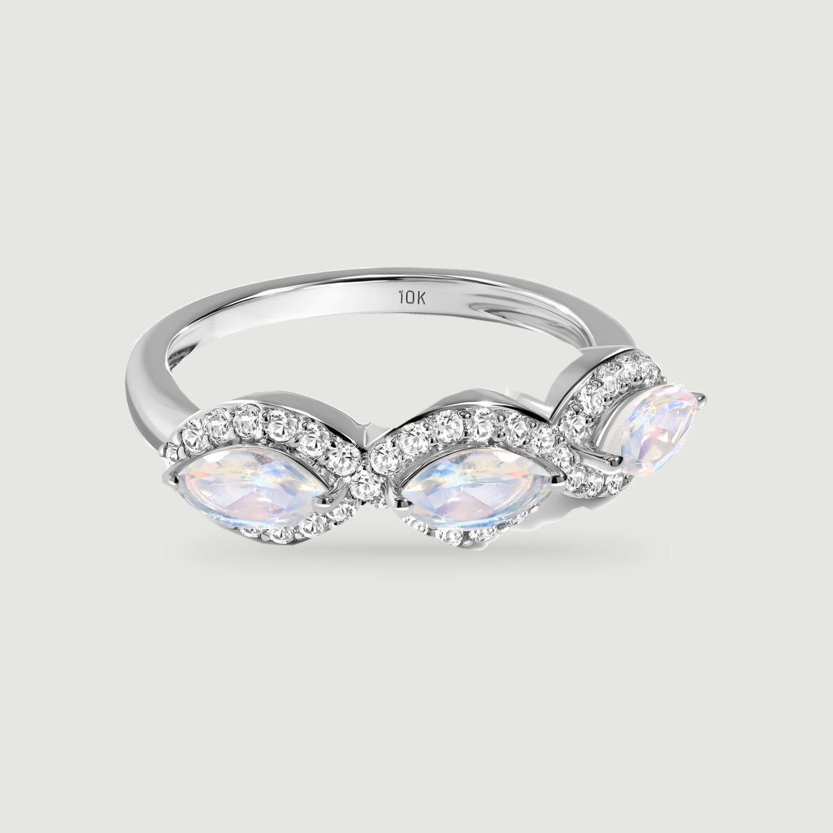 A white gold ring with three marquise moonstones and diamond halos rests on a light gray surface.