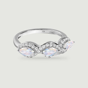 A white gold ring with three marquise moonstones and diamond halos rests on a light gray surface.