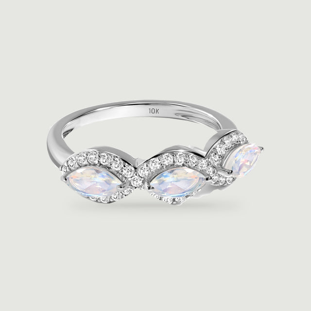A white gold ring with three marquise moonstones and diamond halos rests on a light gray surface.