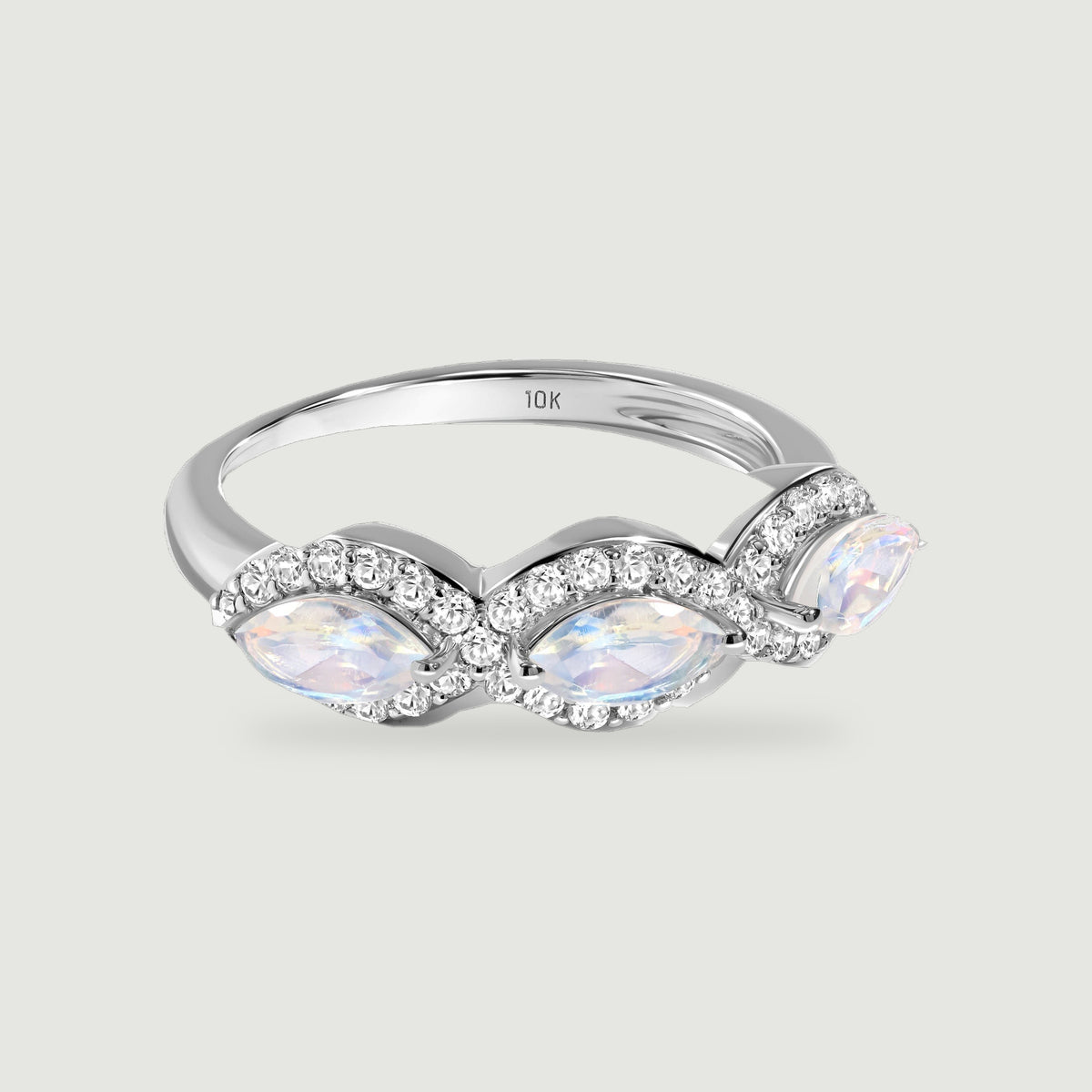 A white gold ring displays three iridescent marquise moonstones with curved diamond borders on a light gray surface.