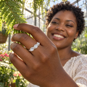 A white gold moonstone ring is worn on a hand reaching toward a fern in a sunlit greenhouse.