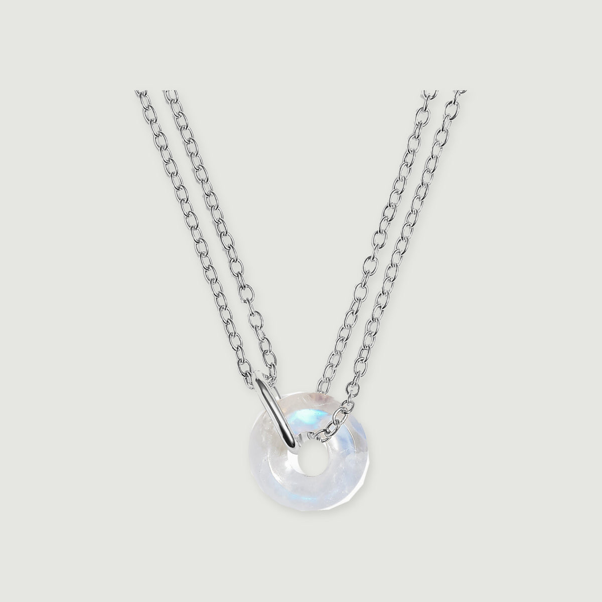 A circular moonstone pendant with a silver connector and double cable chain rests on a pale grey surface.