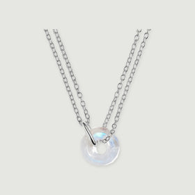 A circular moonstone pendant with a silver connector and double cable chain rests on a pale grey surface.