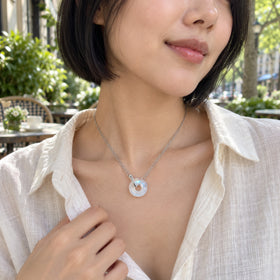 A woman in a cream linen shirt wears a silver double-chain necklace with a round moonstone pendant at an outdoor cafe.