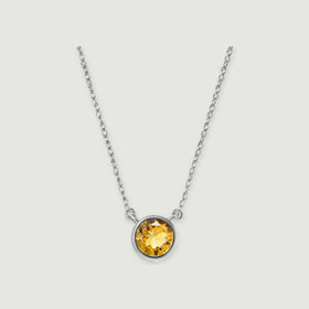 A round golden citrine pendant in a white gold bezel hangs from an oval-link chain against a light grey background.