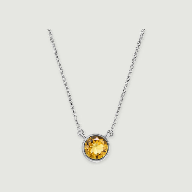 A round golden citrine pendant in a white gold bezel hangs from an oval-link chain against a light grey background.