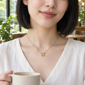A woman with a black bob wears the white gold citrine necklace with an ivory blouse while holding a ceramic cup in a sunlit cafe.