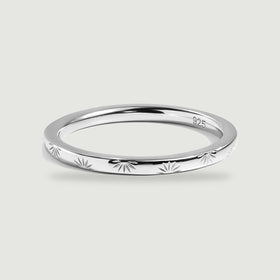 A polished silver band with radiating engravings rests on a light gray surface.