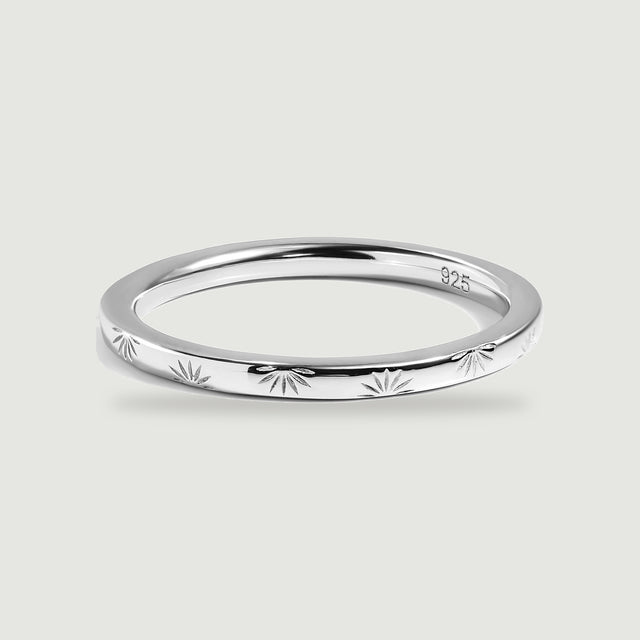 A polished silver band with radiating engravings rests on a light gray surface.