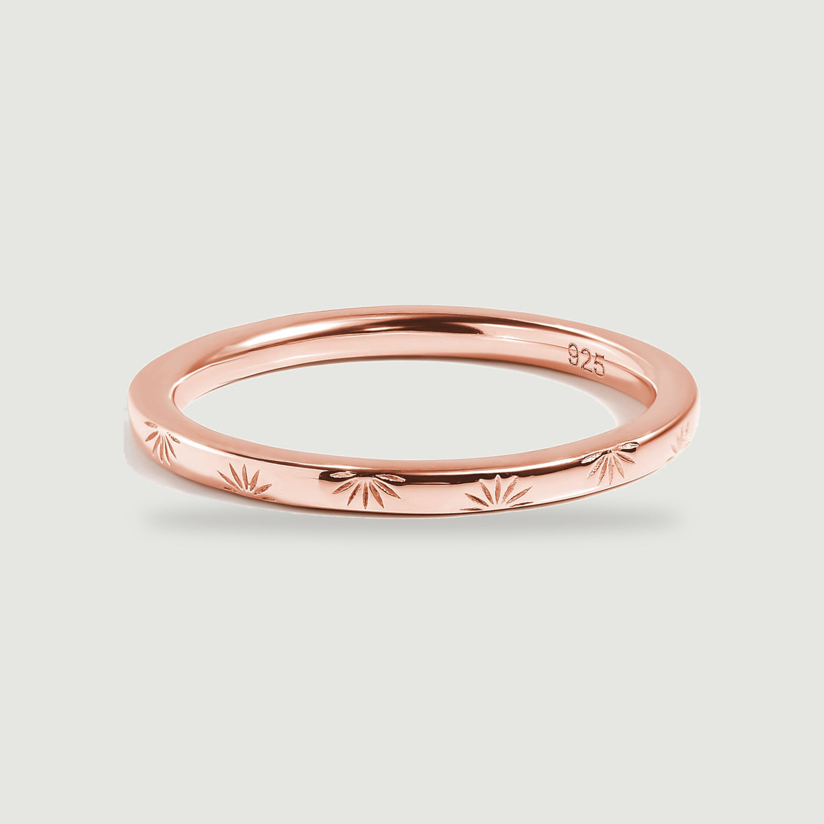 A rose gold band with repeating engraved motifs sits above a soft contact shadow.