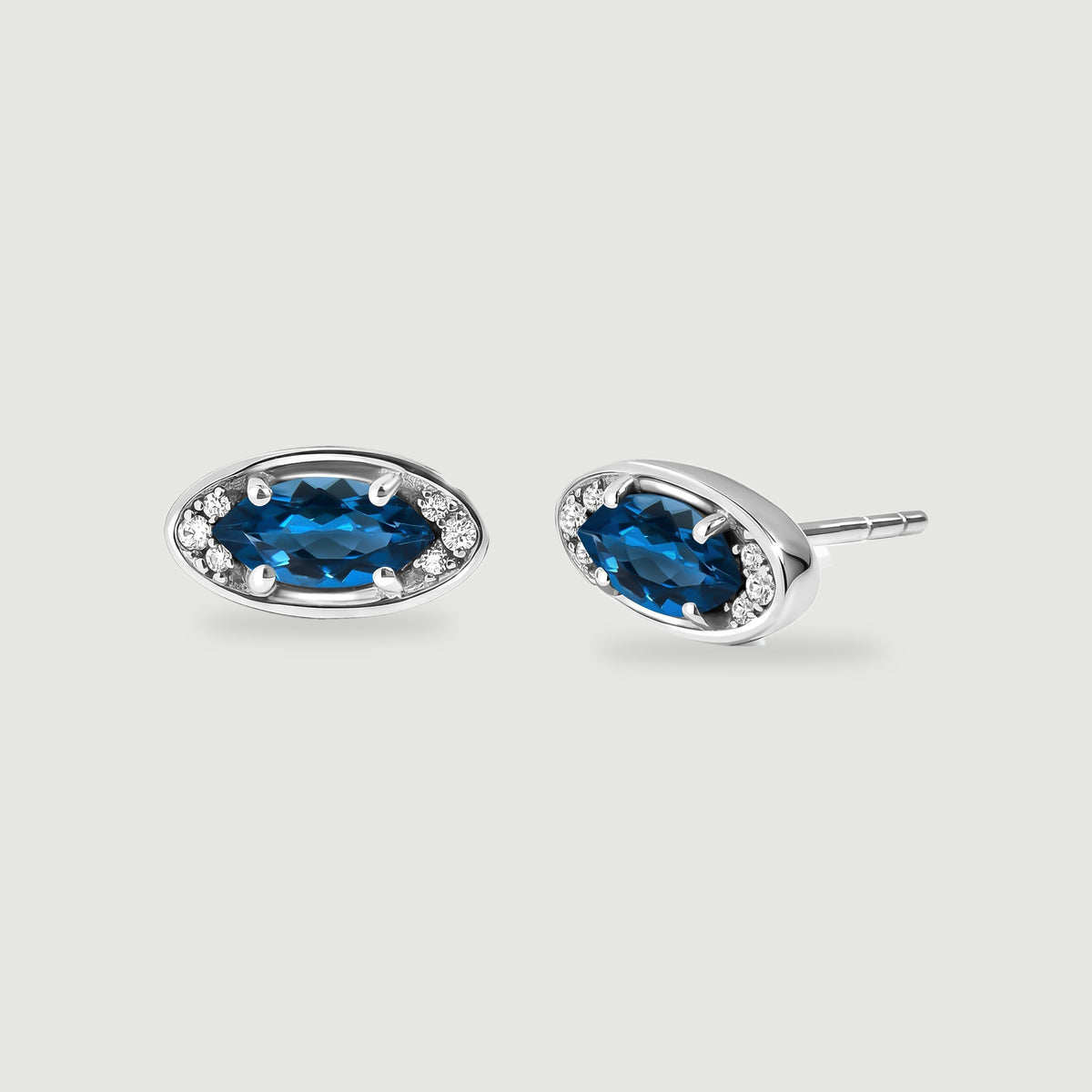 Two silver-tone stud earrings show oval blue stones and clear accents on a light gray background.