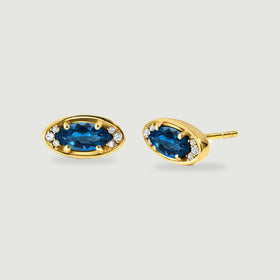A pair of yellow-gold-tone earrings displays faceted blue centers with the rear post visible.