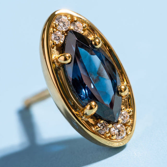 The yellow-gold-tone stud fills the frame with its elongated blue stone and clusters of clear accents.
