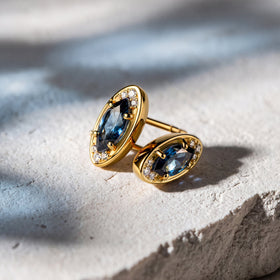 Yellow-gold-tone earrings lie together on a light stone surface with soft directional shadows.