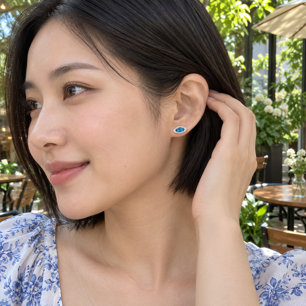A woman with a short black bob wears a silver-tone blue-stone stud at a leafy cafe terrace.