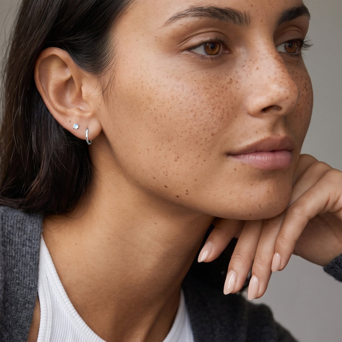 Close-up portrait of a freckled person wearing a small wavy hoop and round stud earring.