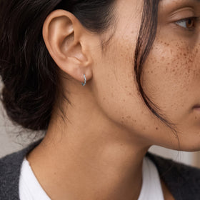 Side profile showing a freckled person wearing a small, undulating hoop earring on one ear.