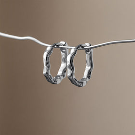 Two sculpted hoop earrings hang from a slender wavy line against a taupe background.