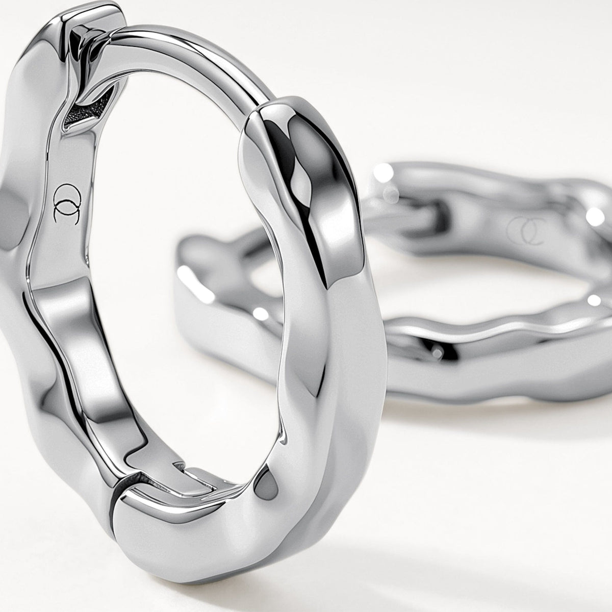 Macro view of a polished wavy hoop earring with a second matching hoop softly blurred behind.