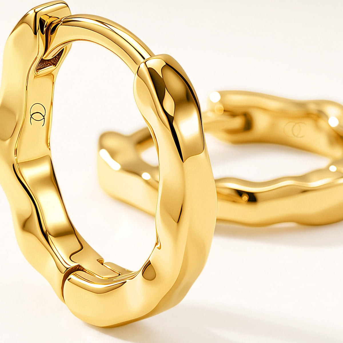 Large foreground hoop earring gleams beside a softly out-of-focus matching hoop on a white surface.